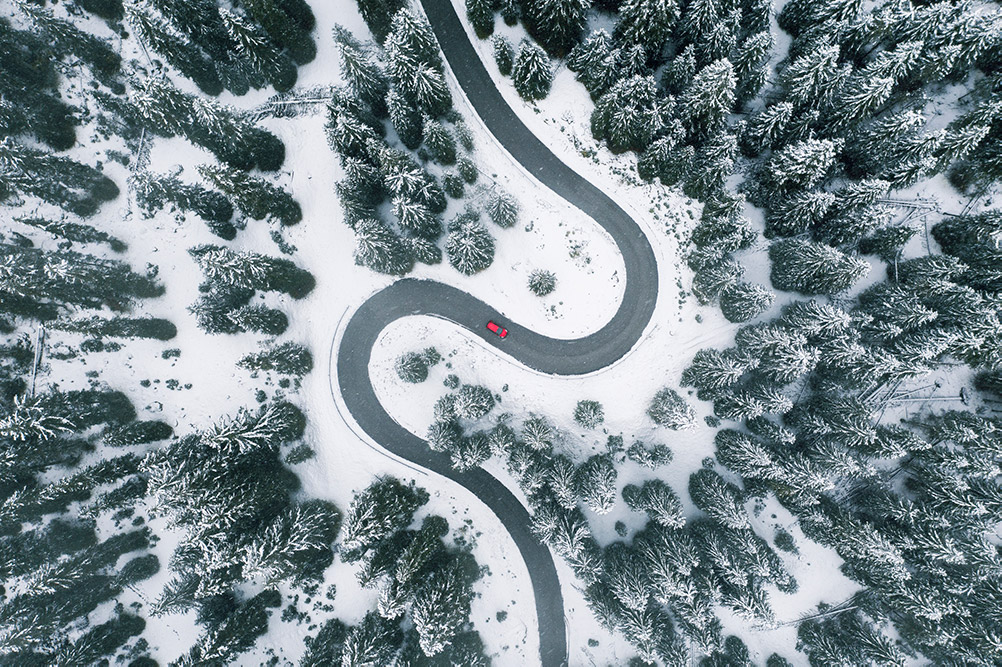 Perspektiv ovanifrån på en röd bil som kör på en skogsväg under vintern.